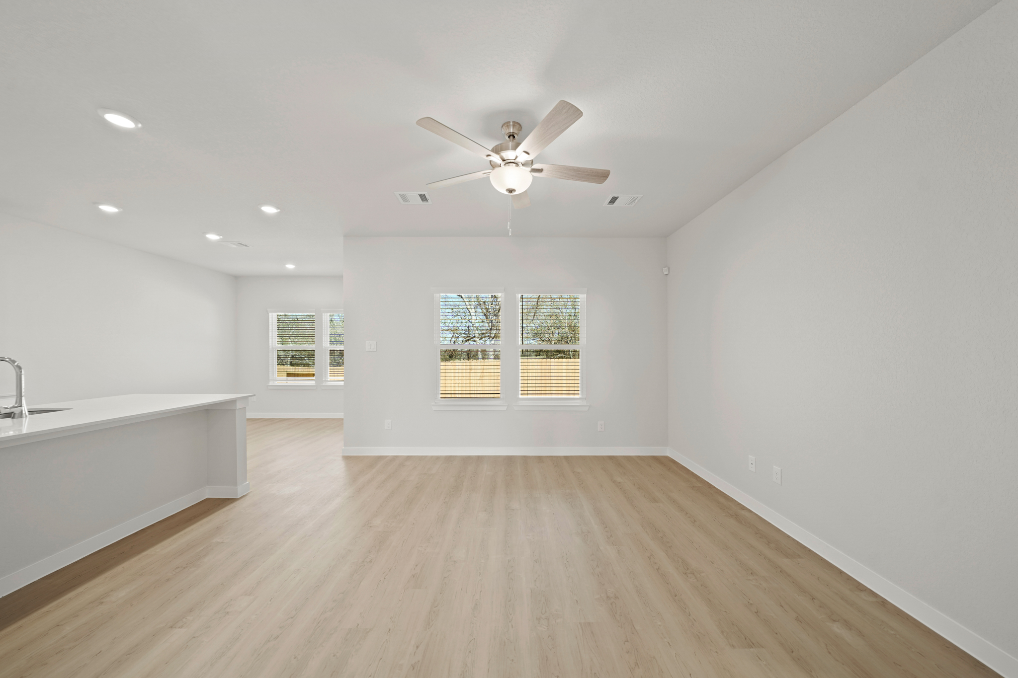 A large empty room with a ceiling fan and a wood floor.